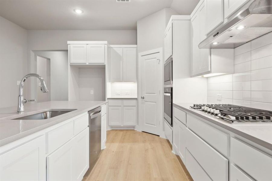 Kitchen with appliances with stainless steel finishes, sink, light hardwood / wood-style flooring, and white cabinets