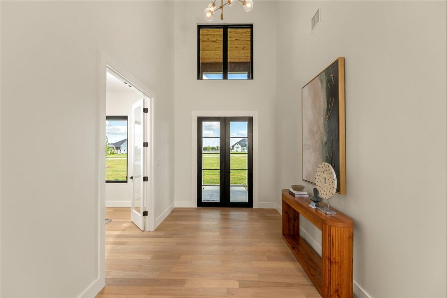 Entryway with light wood finished floors, french doors, a high ceiling, and hanging lights