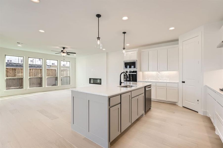 Kitchen with sink, stainless steel appliances, light hardwood / wood-style flooring, an island with sink, and decorative light fixtures