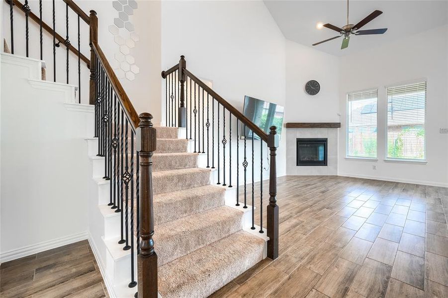 Stairway featuring wood tiled floors, a fireplace, a ceiling fan, and a towering ceiling Stairway featuring wood tiled floors, a fireplace, a ceiling fan, and a towering ceiling
