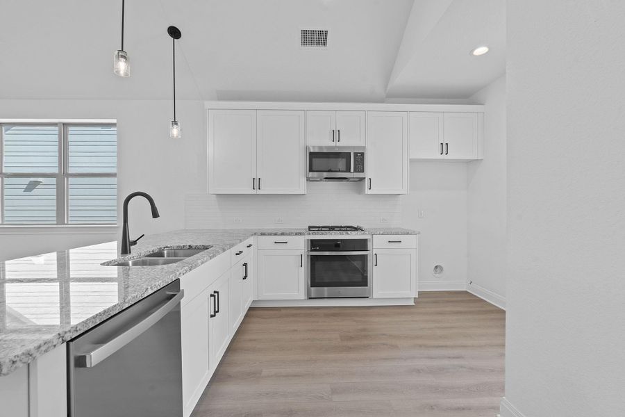 Kitchen with white cabinets, stainless steel appliances, light stone counters, light wood-type flooring, and recessed lighting Kitchen with white cabinets, stainless steel appliances, light stone counters, light wood-type flooring, and recessed lighting