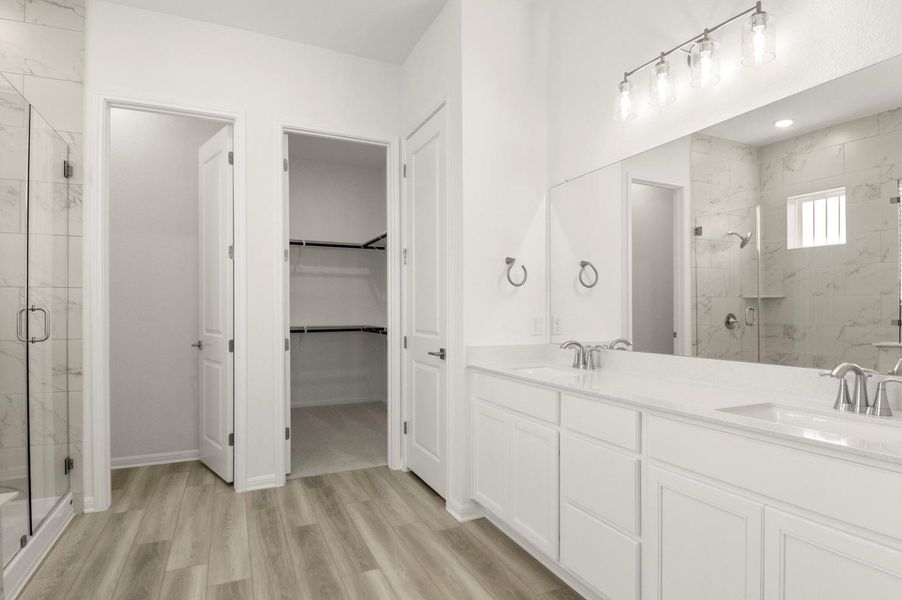 Bathroom featuring a marble finish shower, double vanity, light wood-style floors, and a walk in closet