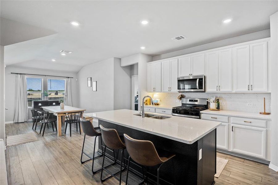 Kitchen featuring a center island with sink, decorative backsplash, recessed lighting, appliances with stainless steel finishes, and light stone counters