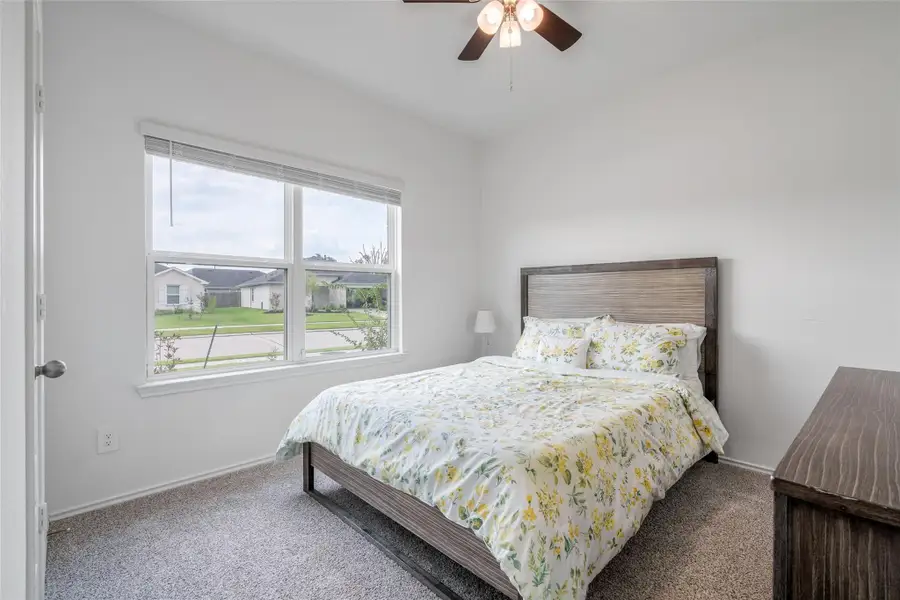 This downstairs bedroom offers comfort and privacy with multiple windows fitted with privacy blinds, a ceiling fan for year-round comfort, and plush carpet flooring for a modern touch. This downstairs bedroom offers comfort and privacy with multiple windows fitted with privacy blinds, a ceiling fan for year-round comfort, and plush carpet flooring for a modern touch.