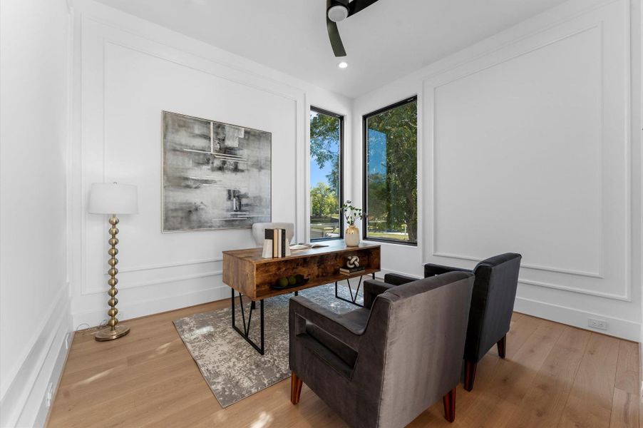 This photo showcases a bright and elegant home office with modern furnishings. It features large windows that allow natural light to pour in, highlighting the sleek desk and comfortable seating. The room has a minimalist design with white walls and light wood flooring, creating a serene and productive atmosphere.