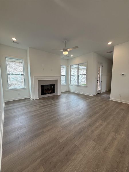 Spacious living area featuring wood-finish flooring, a fireplace with a white mantel, and multiple windows providing ambient light