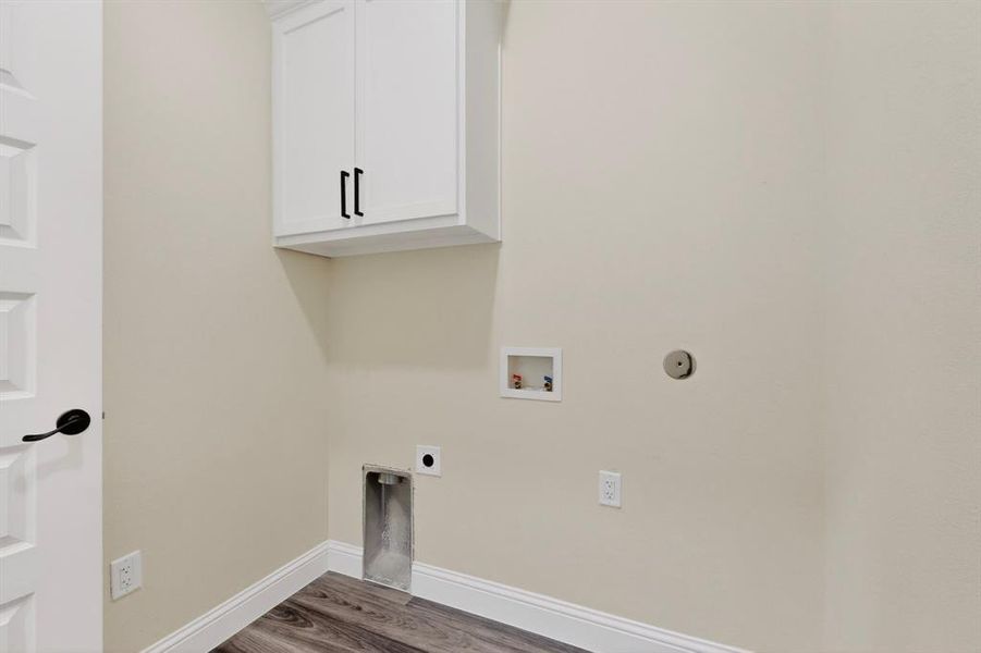 Dedicated laundry space featuring white upper cabinetry with dark hardware, a panel door with dark hardware, wood-finish flooring, and light wall paint
