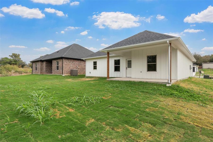 Rear view of property featuring a patio area, roof with shingles, board and batten siding, and a yard