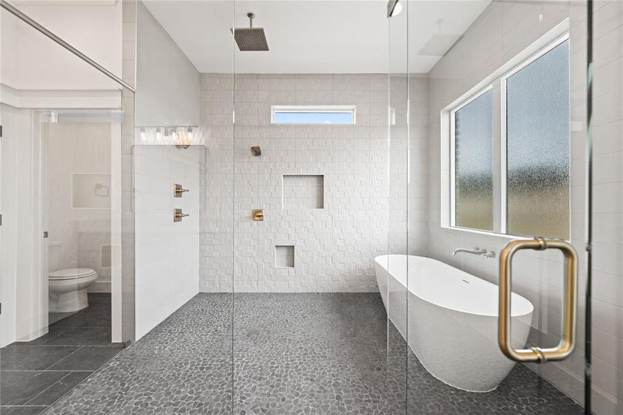 Spacious bathroom featuring a frameless glass shower enclosure with pebble flooring, a freestanding soaking tub, and contemporary wall-mounted fixtures