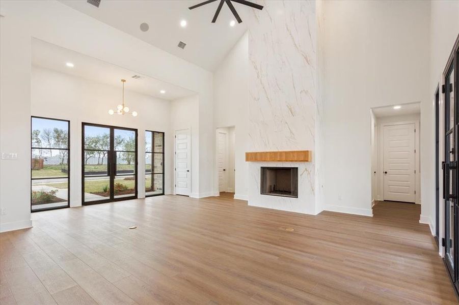 Unfurnished living room with a towering ceiling, a premium fireplace, light wood-type flooring, recessed lighting, and a chandelier