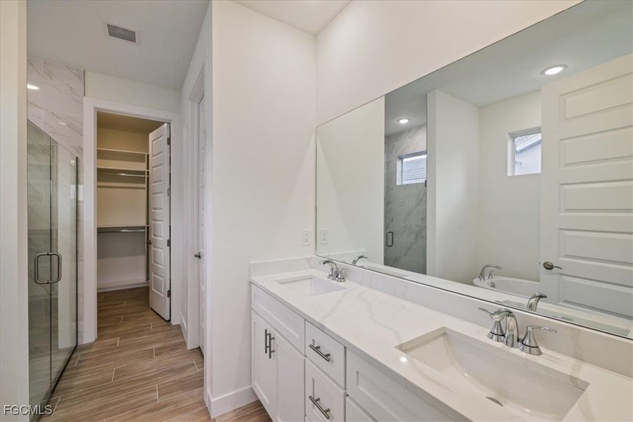Full bath featuring a marble finish shower, double vanity, wood tiled floors, a spacious closet, and a tub to relax in