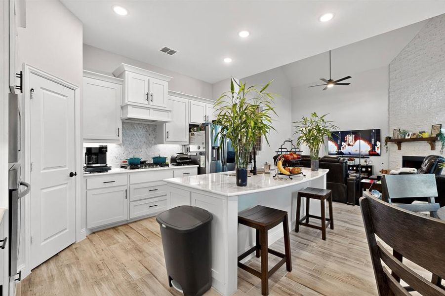 Kitchen with white cabinets, open floor plan, light wood-type flooring, a breakfast bar, and vaulted ceiling Kitchen with white cabinets, open floor plan, light wood-type flooring, a breakfast bar, and vaulted ceiling