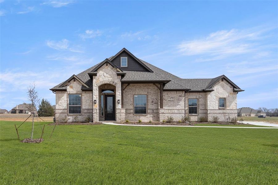 French provincial home featuring roof with shingles, a front yard, stone siding, and brick siding French provincial home featuring roof with shingles, a front yard, stone siding, and brick siding