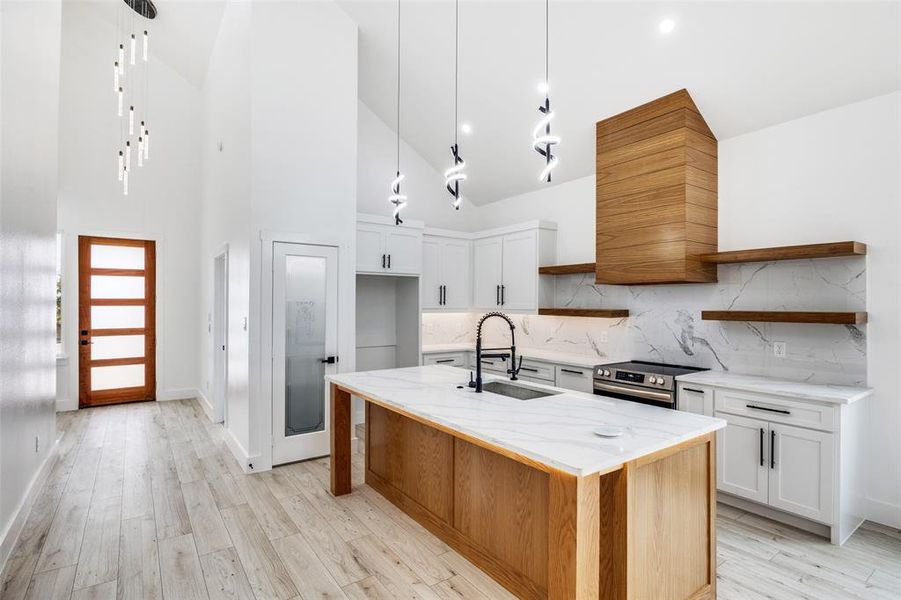 Kitchen with open shelves, light stone countertops, light wood-style floors, high vaulted ceiling, and white cabinetry Kitchen with open shelves, light stone countertops, light wood-style floors, high vaulted ceiling, and white cabinetry