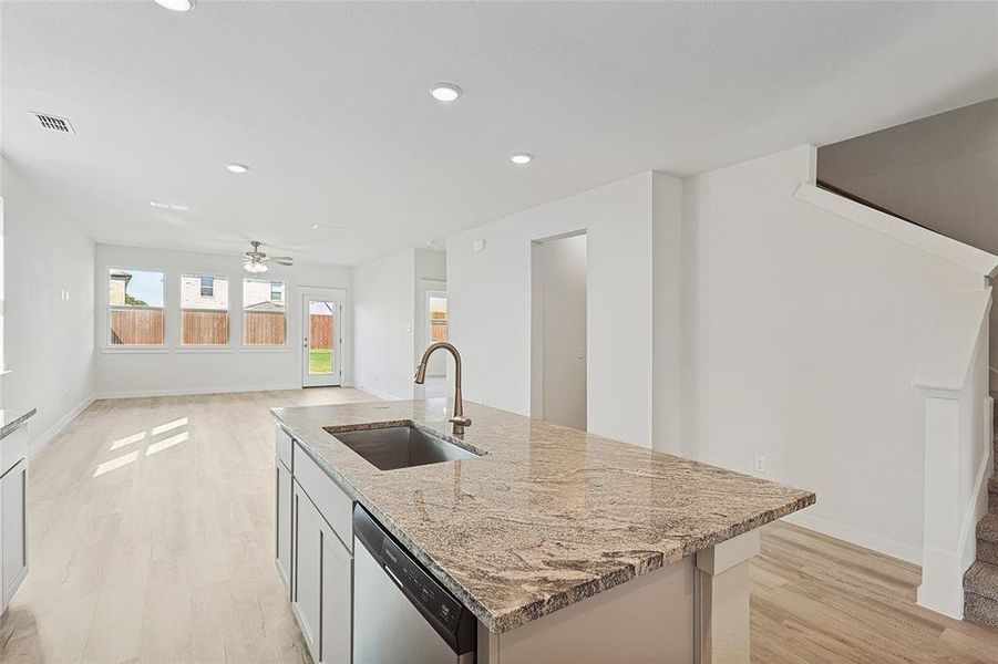 Kitchen featuring stainless steel dishwasher, light stone countertops, sink, and light wood-type flooring