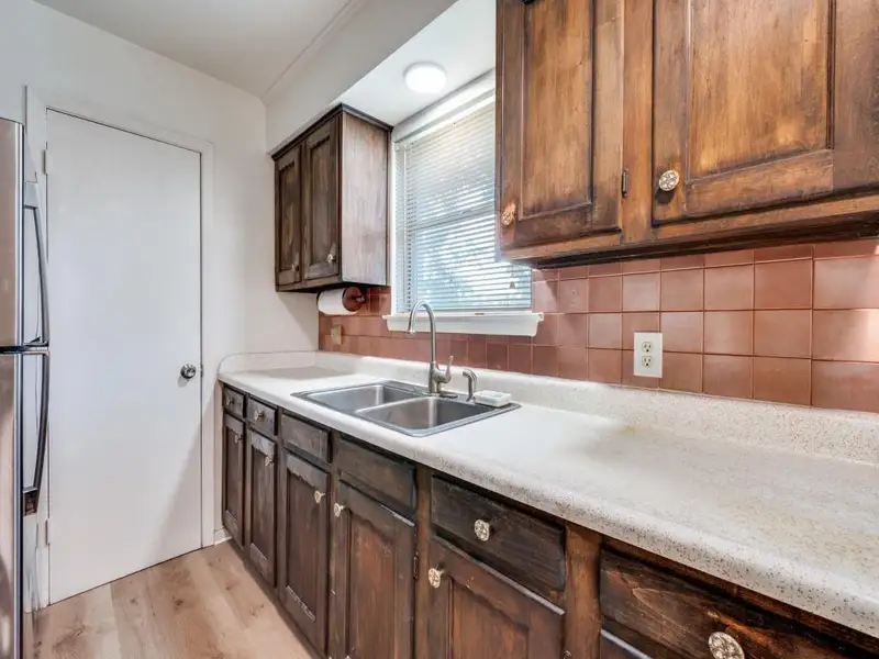 Kitchen with dark brown cabinetry, light wood-style floors, light countertops, freestanding refrigerator, and tasteful backsplash Kitchen with dark brown cabinetry, light wood-style floors, light countertops, freestanding refrigerator, and tasteful backsplash