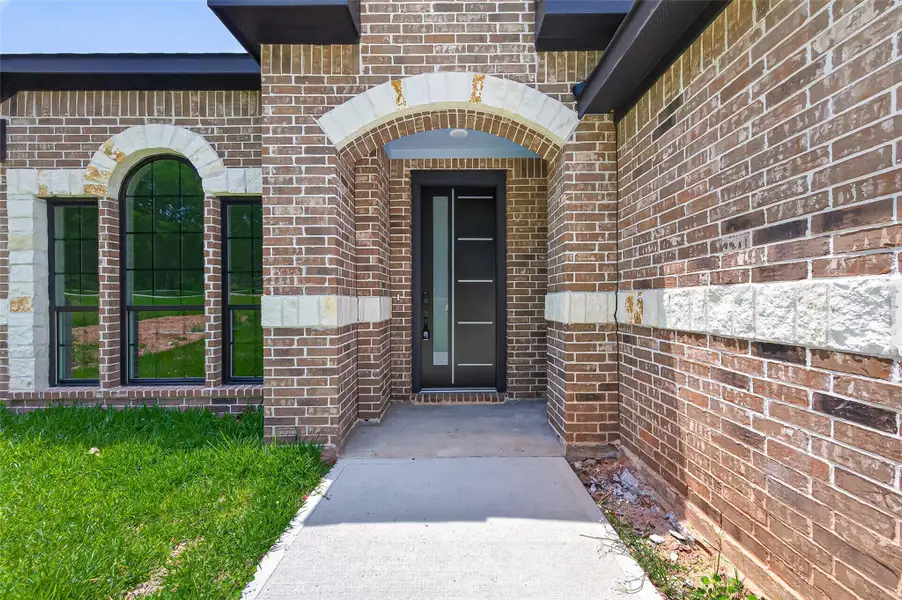 This charming home features a brick exterior with a modern design, including large arched windows and a spacious driveway