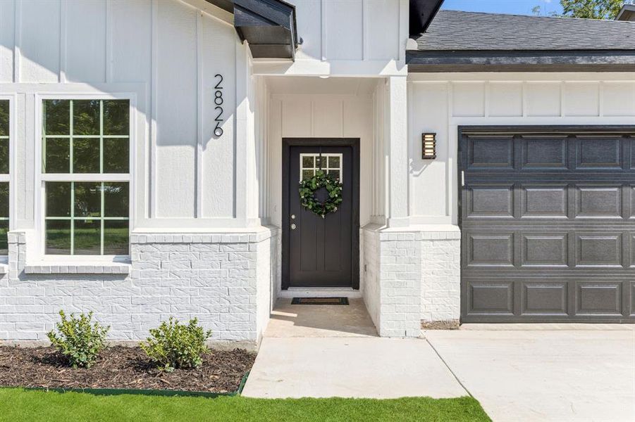Property entrance featuring board and batten siding, a shingled roof, and a garage