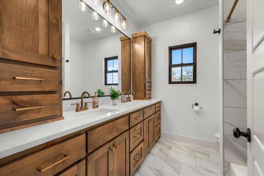 Full bathroom with dual sinks, stained cabinetry with ample storage, quarter countertops and gold finishes.  Full tub and shower combo with toilet in back right.  Located near additional two bedrooms.