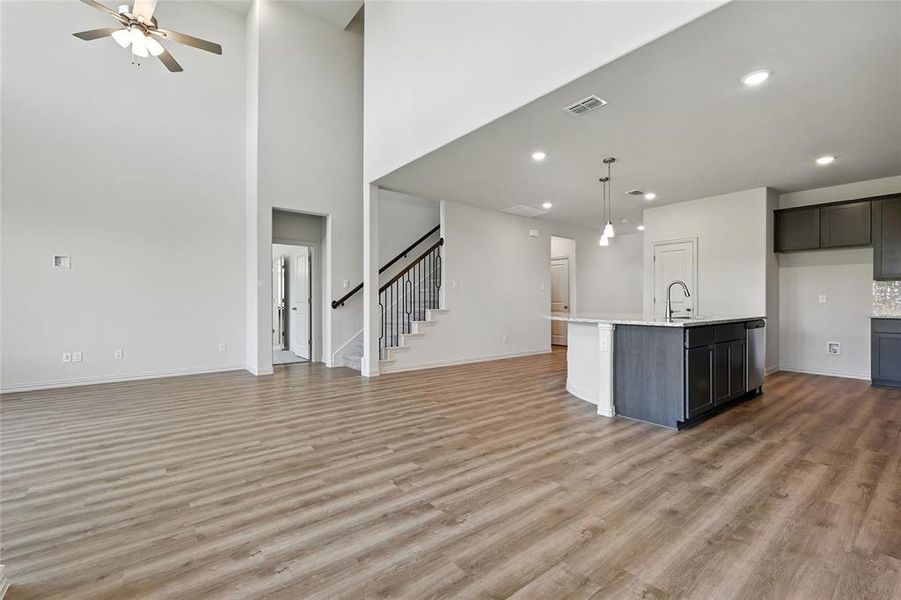 Kitchen featuring open floor plan, a center island with sink, light wood finished floors, hanging light fixtures, and a towering ceiling