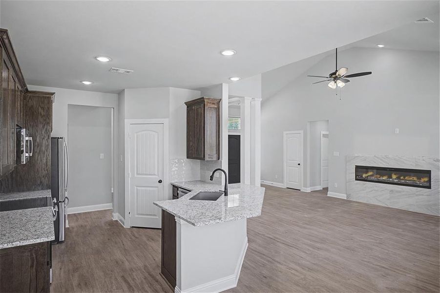 Kitchen featuring a premium fireplace, dark wood finish cabinets, light stone counters, ceiling fan, and light wood-type flooring