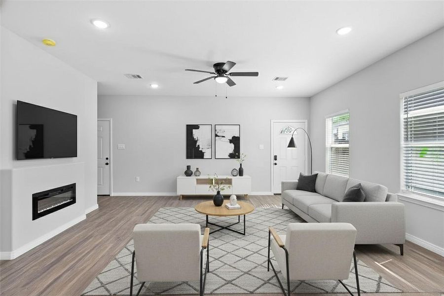 This modern living room features sleek gray walls, wood flooring, and abundant natural light. It includes a cozy seating area with an electric fireplace and a ceiling fan add to the inviting atmosphere. **Photo has been staged.**