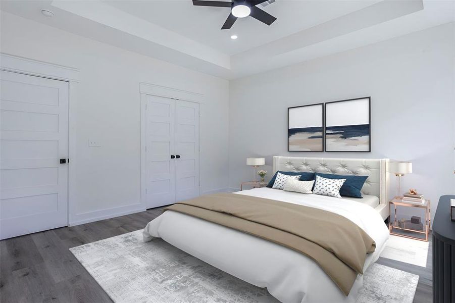 Bedroom featuring light gray walls, wood-finish flooring, a tray ceiling with a ceiling fan, and two paneled doors with dark hardware - virtual staging