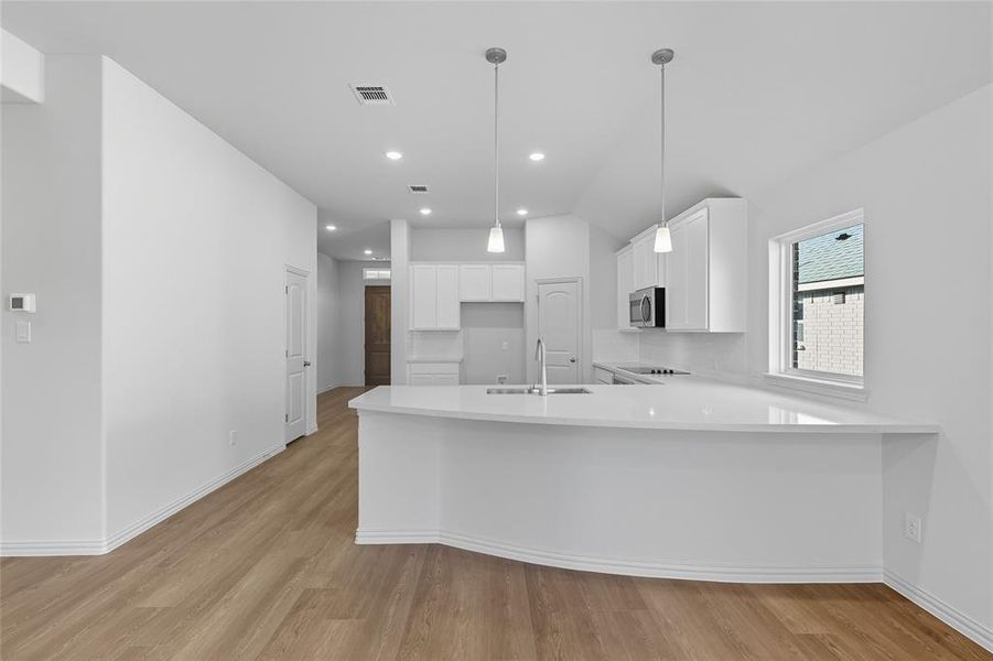 Kitchen with a peninsula, white cabinetry, light wood-type flooring, pendant lighting, and recessed lighting Kitchen with a peninsula, white cabinetry, light wood-type flooring, pendant lighting, and recessed lighting