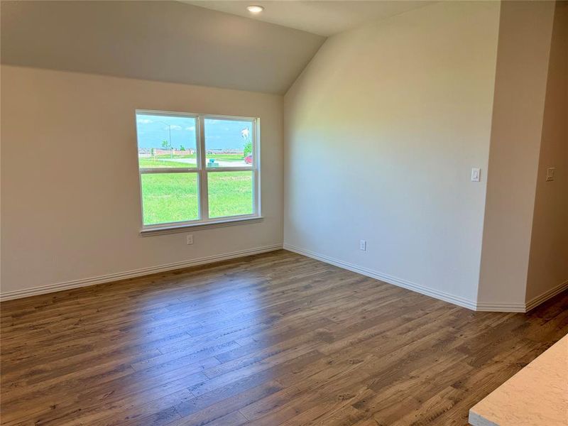 Spacious room featuring wood-finish flooring, a large window, vaulted ceiling, recessed lighting, and crisp white baseboards