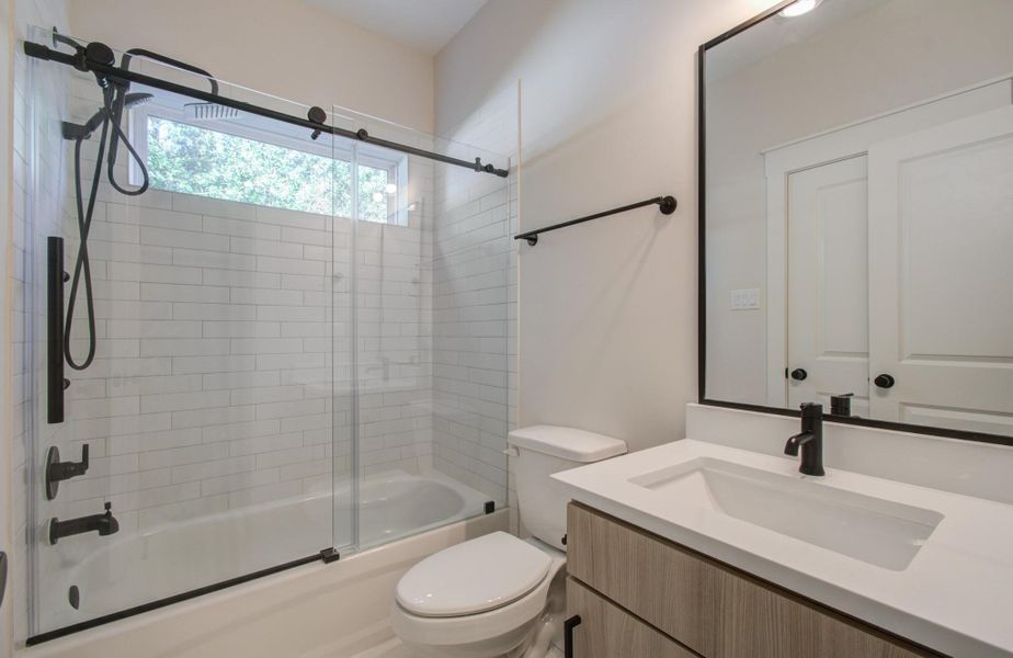 Step into a guest bathroom that feels like a private spa. This beautifully appointed space features a shower/tub combination with a custom sliding glass door, accented by premium hardware and sleek tilework. The true highlight? A luxurious rainforest showerhead that offers a relaxing, full-body experience—transforming every rinse into a rejuvenating retreat.