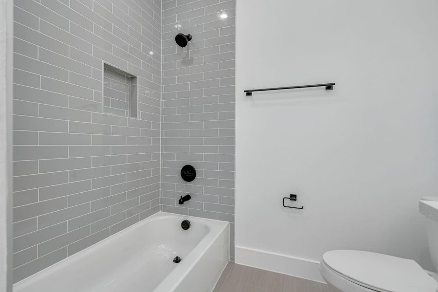 Primary bath tub and shower combo with floor-to-ceiling gray subway tile, built-in niche, and modern black fixtures for a clean contemporary look.