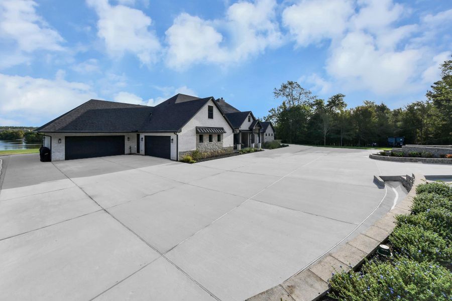 Expansive modern home with a spacious driveway and a beautiful lakeside view, surrounded by lush trees for added privacy.