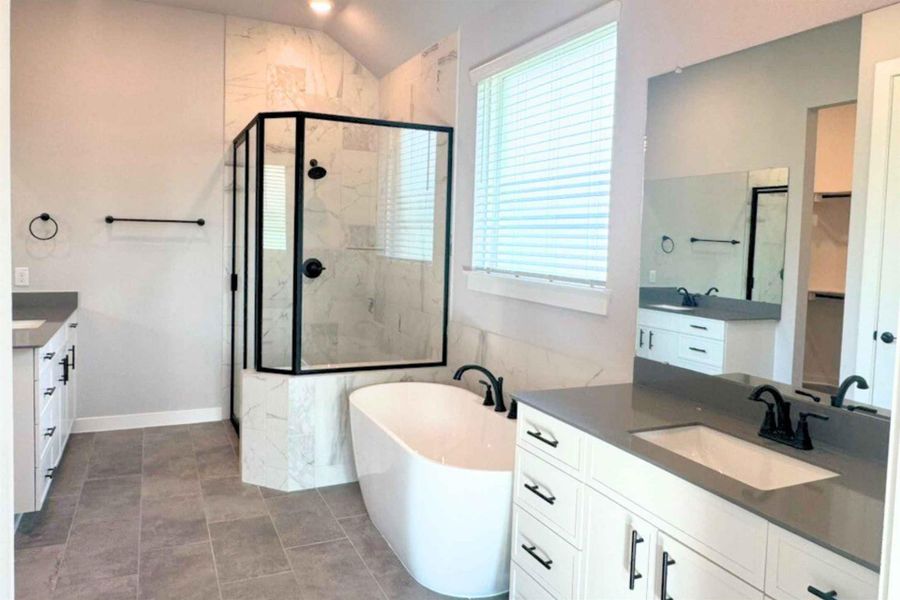 Bathroom with a shower stall, a freestanding bath, two vanities, lofted ceiling, and light tile patterned floors Bathroom with a shower stall, a freestanding bath, two vanities, lofted ceiling, and light tile patterned floors