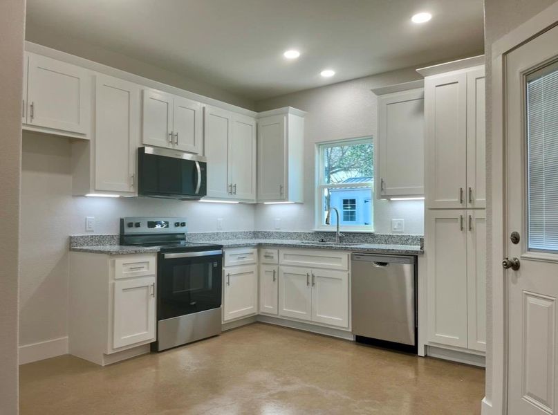 Kitchen featuring appliances with stainless steel finishes, white cabinets, light stone countertops, concrete floors, and recessed lighting