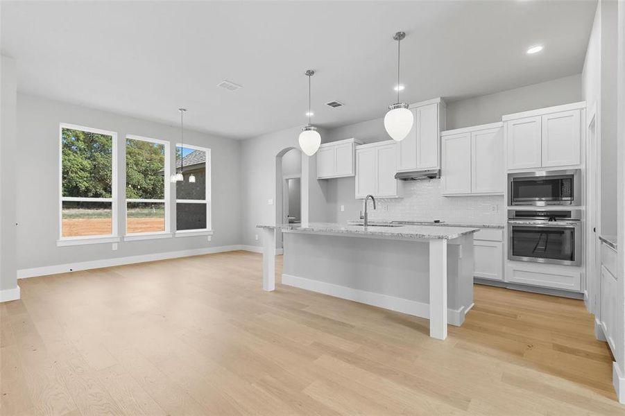Kitchen with arched walkways, stainless steel appliances, white cabinets, a center island with sink, and decorative backsplash