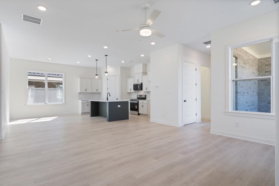 Open-concept space featuring wood-finish flooring, a central kitchen island with a matte black faucet, shaker-style cabinetry, recessed ceiling lighting, and a multi-blade ceiling fan Open-concept space featuring wood-finish flooring, a central kitchen island with a matte black faucet, shaker-style cabinetry, recessed ceiling lighting, and a multi-blade ceiling fan