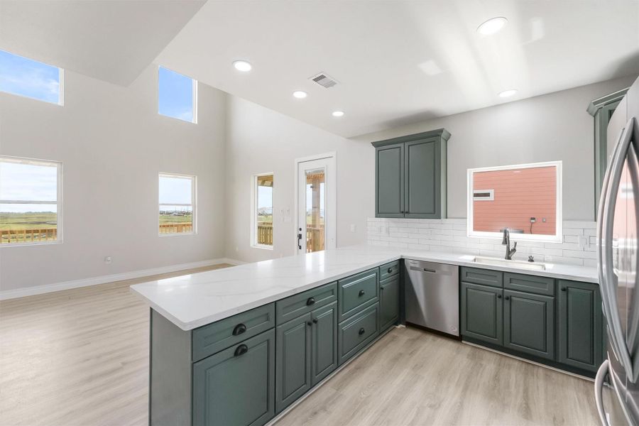 A modern kitchen with sleek, dark cabinetry, white countertops, and stainless steel appliances. It opens up to a spacious area with high ceilings and large windows, offering plenty of natural light and scenic views. A modern kitchen with sleek, dark cabinetry, white countertops, and stainless steel appliances. It opens up to a spacious area with high ceilings and large windows, offering plenty of natural light and scenic views.