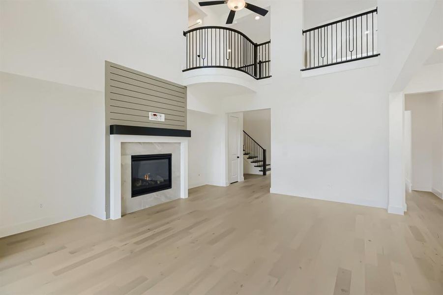 Two-story living area featuring light wood-finish flooring and a fireplace with a white mantel, stone-look surround, and shiplap-style accent wall Two-story living area featuring light wood-finish flooring and a fireplace with a white mantel, stone-look surround, and shiplap-style accent wall