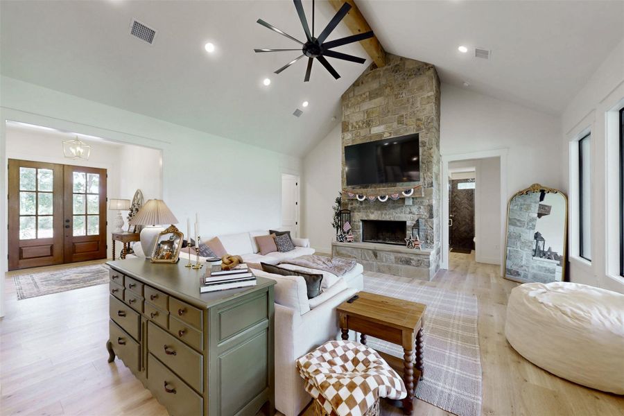 Living area featuring beamed ceiling, light wood-style flooring, a fireplace, high vaulted ceiling, and french doors