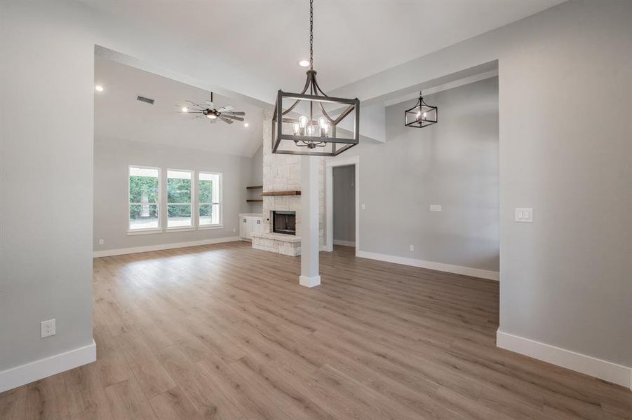 Unfurnished living room with ceiling fan with notable chandelier, a fireplace, vaulted ceiling, and light hardwood / wood-style floors