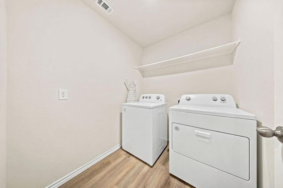 Dedicated laundry area featuring wood-finish flooring, a white floating shelf, and white baseboards Dedicated laundry area featuring wood-finish flooring, a white floating shelf, and white baseboards