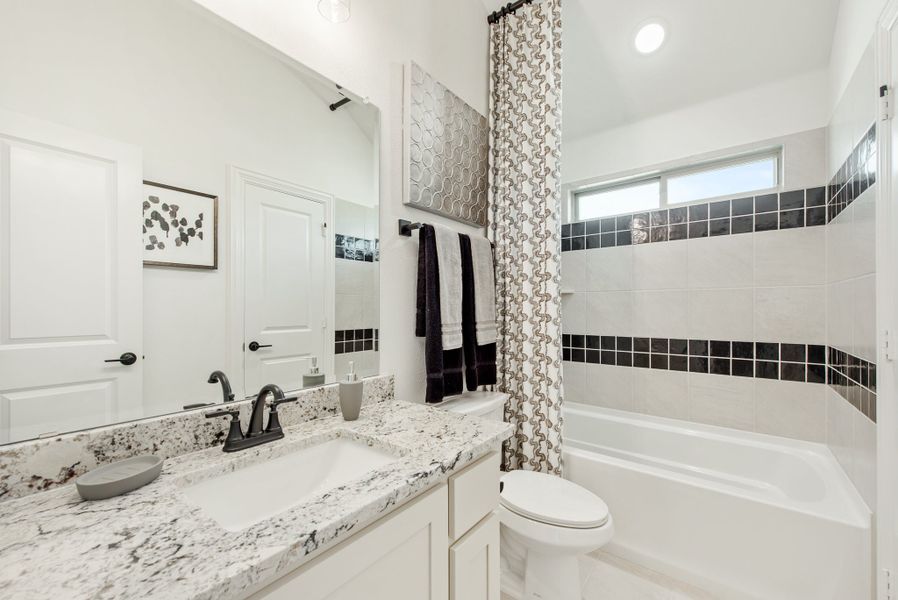 Bathroom with granite countertop, white cabinets, and tiled bathtub with dark accent tiles Bathroom with granite countertop, white cabinets, and tiled bathtub with dark accent tiles