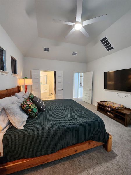 A tranquil primary bedroom suite featuring a vaulted ceiling, soft carpet, and convenient access to a private bathroom.