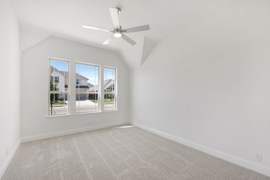 Empty bedroom with vaulted ceiling, ceiling fan, carpet flooring, and three windows with neighborhood view