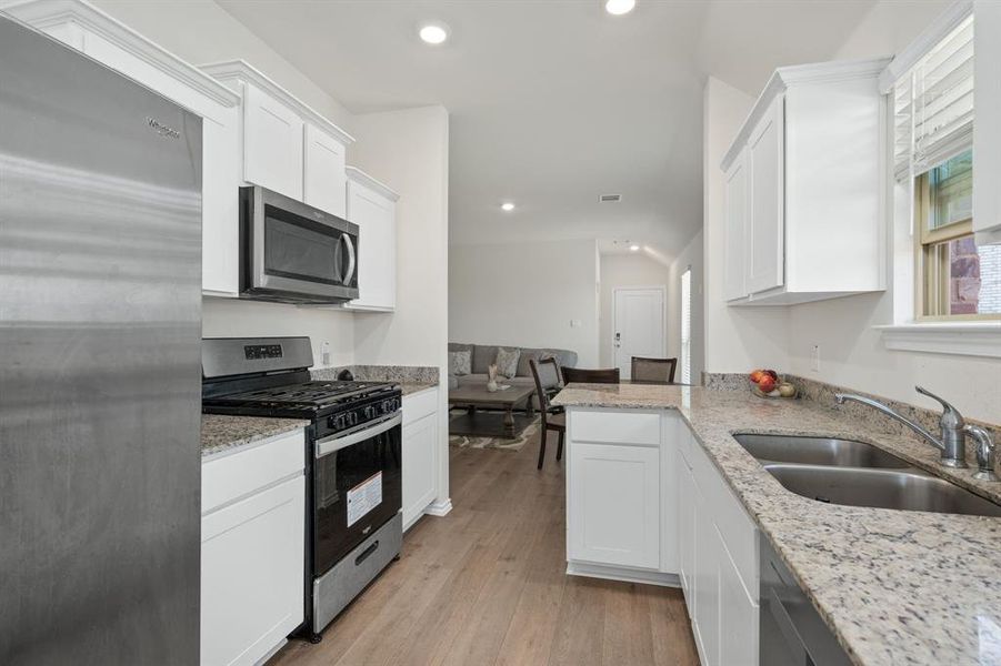Kitchen with appliances with stainless steel finishes, light stone counters, light wood-style flooring, white cabinetry, and recessed lighting Kitchen with appliances with stainless steel finishes, light stone counters, light wood-style flooring, white cabinetry, and recessed lighting