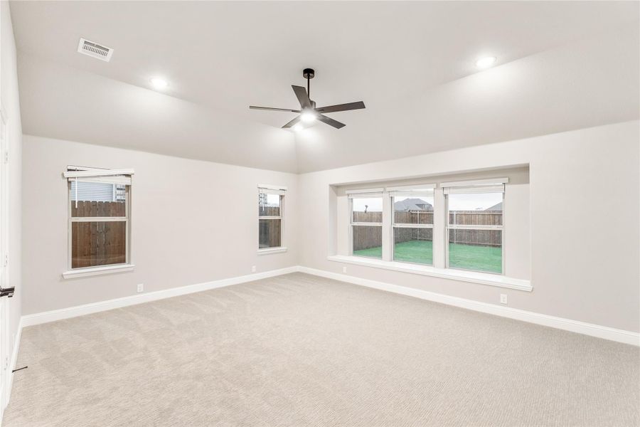 Spacious empty room with carpet, ceiling fan, recessed lighting, and three windows overlooking a fenced backyard.