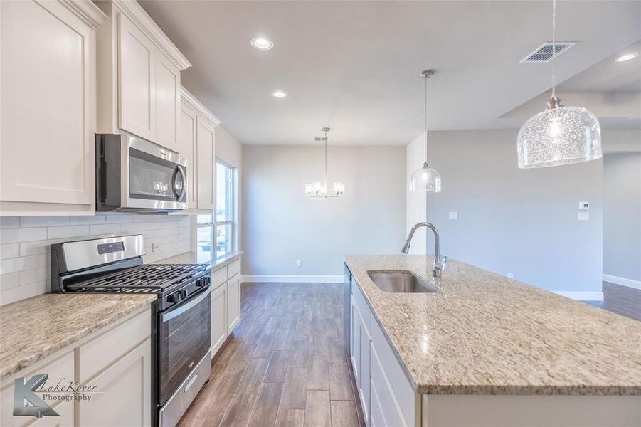 Kitchen with stainless steel appliances, dark wood finish ceramic tile floors, white cabinets, recessed lighting, and decorative light fixtures