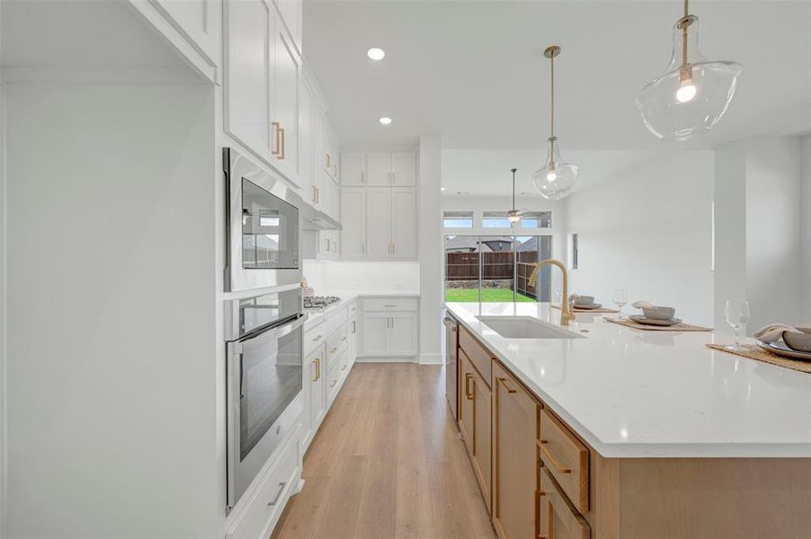 Kitchen featuring a spacious island with a white countertop and undermount sink, brass-finish faucet, and wood-finish cabinetry
