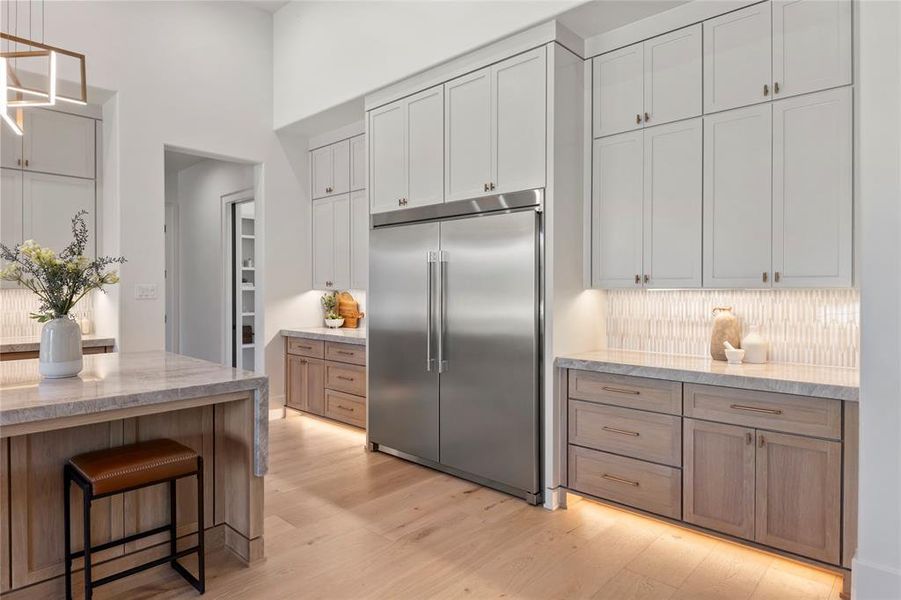 Kitchen featuring built in refrigerator, light stone counters, light wood-style flooring, backsplash, and pendant lighting