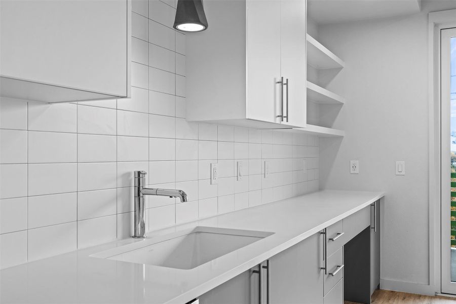 Kitchen with open shelves, light countertops, backsplash, and a sink